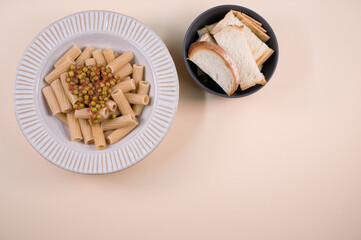 Poster - Top view of rigatoni pasta with green peas and slices of bread isolated on brown background