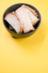 Poster - Vertical shot of bread slices on a bowl isolated on yellow background