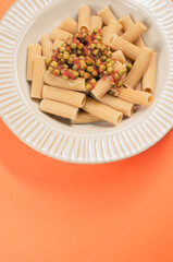 Sticker - Vertical shot of rigatoni pasta with green peas on a plate isolated on an orange background