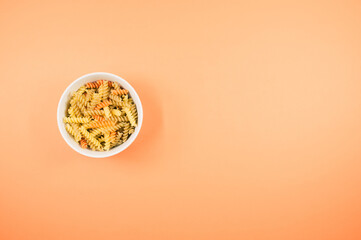 Poster - Top view of uncooked tri-color rotini pasta on a bowl isolated on an orange background