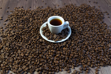 roasted aroma coffee beans on brown wooden table, in white saucer and cup with fresh coffee