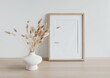 © irenastar - Wooden frame mockup on beige table, modern beige ceramic vase with dry grass.Neutral color. White wall background. Scandinavian interior. Copy space.