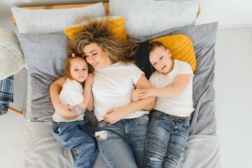 Portrait of smiling young mommy embracing kids little son and daughter. Happy family. Mother with children sitting on bed and loving the good times together. Closeup