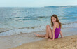 Teen girl sits on sand near sea