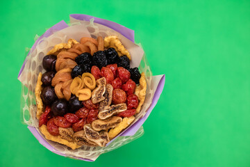 Decorative composition in the form of a bouquet of dried fruits and nuts on a green background