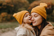© Ananass - Young happy and smiling mom with her little daughter in arms hugging and kissing spending a weekend on a walk in autumn park. selective focus, noise effect, Autumnal mood
