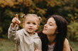 © Ananass - Young happy and smiling mom with her little daughter in arms hugging and kissing spending a weekend on a walk in autumn park. selective focus, noise effect, Autumnal mood