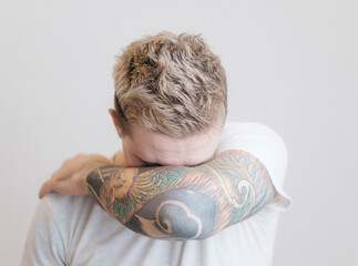 Portrait of a modern young guy with a tattoo on his arm. The man covers himself from the camera with his hand.