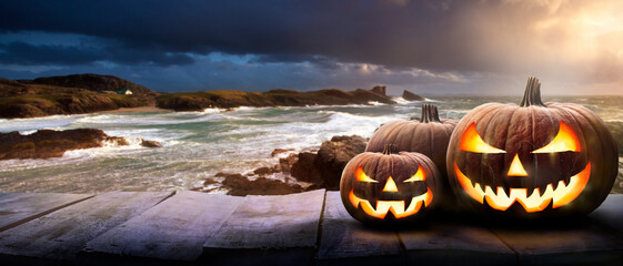 Wall Mural - sunset at the coast with the spooky evil glowing eyes of jack o' lanterns on the right of a wooden b