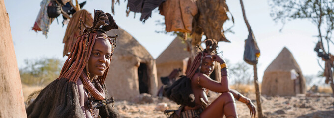 Panoramic shot showing Himba tribeswomen sitting outside their huts in a traditional Himba village near Kamanjab in northern Namibia, Africa.