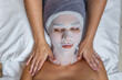 Woman with her face covered with gauze for skin treatment receiving shoulders massage by beautician