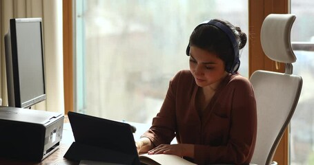 Canvas Print - Indian student in headphones sit on ergonomic office chair writes, study on pc while talk by video call to online teacher use digital tablet. Generation use modern tech for e-learn or business concept