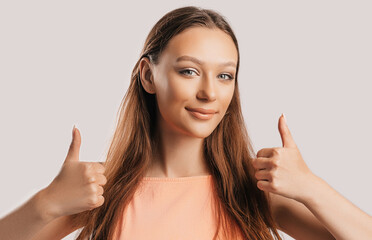 Beautiful young girl smiling and shows thumbs up gesture with two hands on a white isolated background. Positive woman points to an idea, a place for advertising