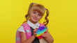 © Andrii Iemelianenko - Joyful pupil girl playing with pop it sensory anti-stress toy. Kid presses on colorful squishy bubbles. Stress and anxiety relief. Yellow studio background. Trendy fidgeting game for stressed children