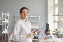 Portrait Of Happy Satisfied Diagnostic Laboratory Scientist Against Copy Space Workplace Background. Medical Specialist In Lab Coat And Goggles Holding Blood Test Tube, Smiling And Looking At Camera