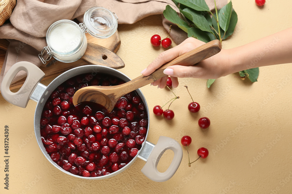 Woman preparing tasty cherry jam on color background