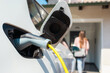 © 24K-Production - Woman charging electric car at home with cable.