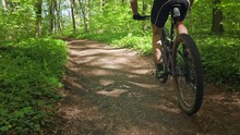 A Man Is Training On An MTB Bike. He Is Driving Fast Along A Path In The Woods. He's Wearing Cycling Clothes. The Camera Is Following Him From Behind. 4K