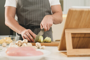 Man cutting zucchini while watching online cooking course via tablet in kitchen, closeup