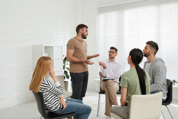 Psychotherapist working with group of drug addicted people at therapy session indoors