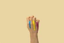 Grabbing Hand With Leaking Drops Of Blue, Yellow, Blue And Pink Paint On Champagne Background