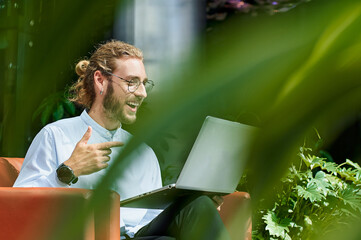 Young businessman laughs during a zoom call in a modern office.