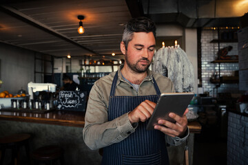 Wall Mural - Caucasian waiter scrolling through online menu standing in trendy cafe preparing orders.