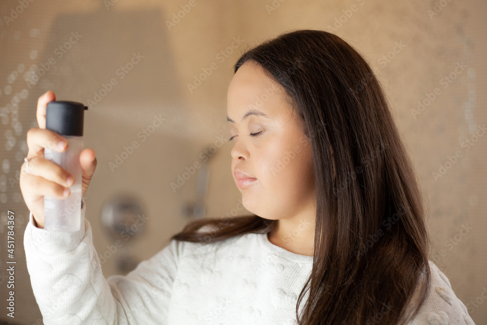 Young biracial woman with Down Syndrome applying make-up setting spray in the bathroom