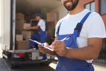 Moving Service Workers Outdoors, Unloading Boxes And Checking List