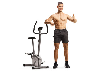 Canvas Print - Shitless fit man leaning on an exercise bike and gesturing a thumb up sign