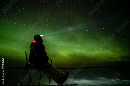A person bundled up in the cold sits and enjoys the night light show of starlight and northern lights (Aurora Borealis).
