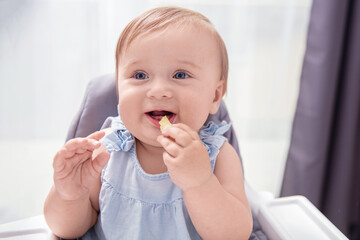 Infant baby girl in blue dress eats crisp and smiles