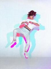 Wall Mural - Dancing mixed race young girl in colourful neon studio light. Female dancer performer jumping hip hop dance