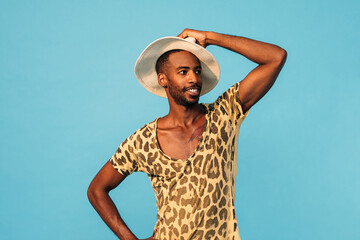 Smiling guy wearing a stylish t-shirt and straw hat looking away while standing against blue background