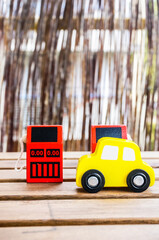 Wall Mural - Vertical shot of a wooden yellow toy car in front of two red wooden gas pump toys