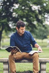 Wall Mural - Vertical shot of a young Caucasian man reading the Bible while sitting on a bench