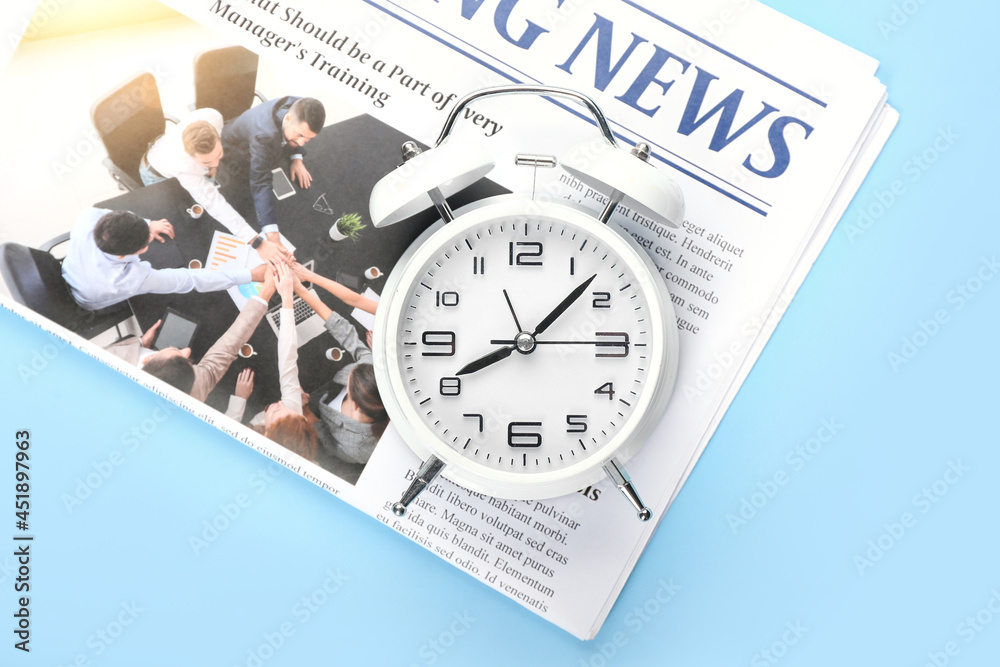 Stylish alarm clock and newspaper on color background