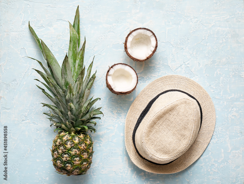 Stylish hat, pineapple and coconut on color background