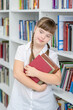 Young girl with syndrome down stands at library and holds books. Education for disabled children concept
