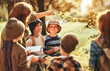 © JenkoAtaman - Children listening to teacher and looking at green leaf while having ecology lesson in forest outdoor