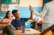 © Drazen - Happy black elementary student and his teacher greet with high five gesture during class at school.