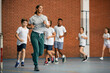 © Drazen - Physical education teacher and group of elementary students run while warming up at school gym.