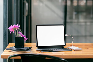 Blank screen tablet with keyboard on wooden table in modern office room.