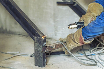 Canvas Print - Man welder assembles a metal staircase structure in a residential building using a welding machine.