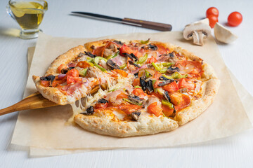 Poster - Tasty delicious traditional italian whole pizza with tomatoes, mushrooms, meat and cheese prepared for eating, sliced and served om white wooden background on craft paper with olive oil. Horizontal