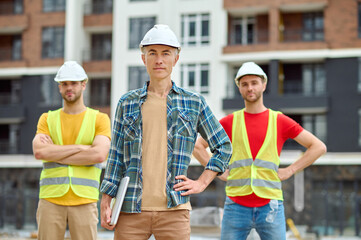 Poster - Three men in protective helmets standing on the building site