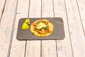 Corn tortilla with Mexican taco al pastor stew with fresh parsley and cilantro, two pieces of green lime, pineapple and onion on black slate