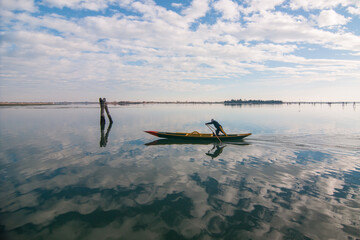 Wall Mural - Person riding a boat on reflective water under a cloudy sky in Venice, Italy