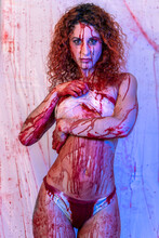 Attractive Bloody Woman With Bandages Covering Her Chest In A Room With Blood Splattered On The Walls
