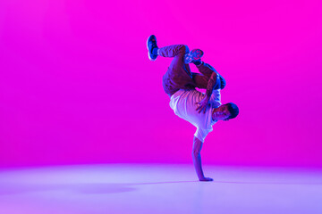 Wall Mural - Young stylish man, break dancing dancer practicing solo in modern clothes isolated over bright magenta background at dance hall in neon light.